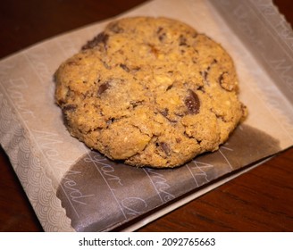 A Big Chocolate Chip Cookie Placed On A Butter Paper Packet. Wooden Background. 