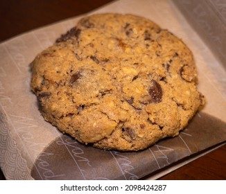 A Big Chocolate Chip Cookie Placed On A Butter Paper Packet.