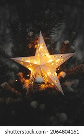 Big Christmas star glowing on snowy pine tree in winter park at night, close up. Atmospheric magic winter time. Illuminated christmas star in evening. Merry Christmas! Xmas miracle