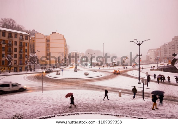 big city covered in snow.\
People walking through the snow city. Traces of cars through the\
snow.