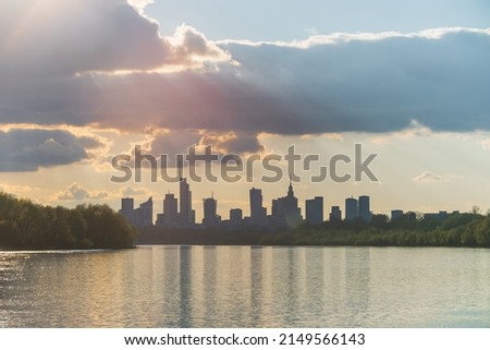 Big city skyline sunny cloudy day in Warsaw, Poland in spring, high buildings skyscrapers on horizon over Wisla river surface. Downtown beautiful cityscape panorama lit with warm sunset light