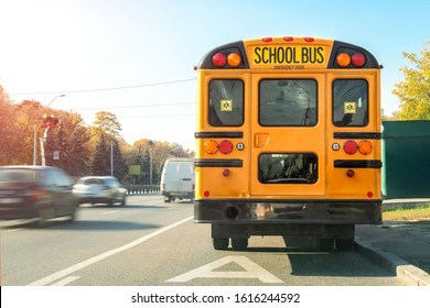 Big Classic Vintage American Yellow Schoolbus Standing On A Bus Lane At Highway And Waiting Pupils And Children For School Trip Road. School Bus Transport Back Door View On Route Bright Morning Time