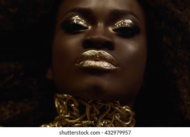 Big close-up surreal portrait of majestic african american female model with gold glossy makeup. Fashion Vogue concept