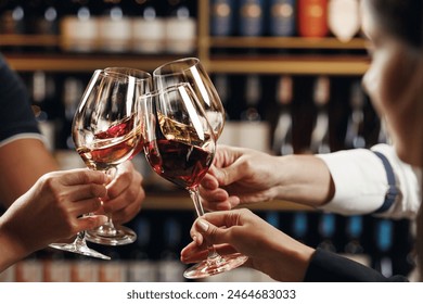 Big company people clinking glasses with red, rose and white wine on blurred cellar background. Men and women cheers with alcohol drink, closeup