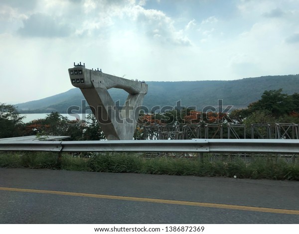Big concrete post in\
nature background.  Construction of motorway road near river and\
mountain backdrop.Motorway construction zone.Large concrete post on\
sky background.