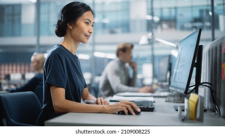 In Big Corporate Office: Portrait of Confident Beautiful Asian Manager Using Computer, Businesspeople and Experts Working Around Her, Analysing Statistics, Commerce Data, Marketing Plans.
