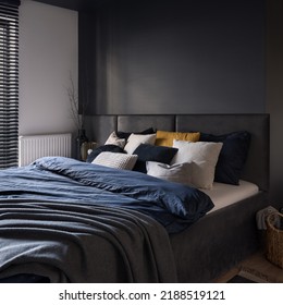 Big and cozy bed in modern and dark bedroom with gray wall and headboard