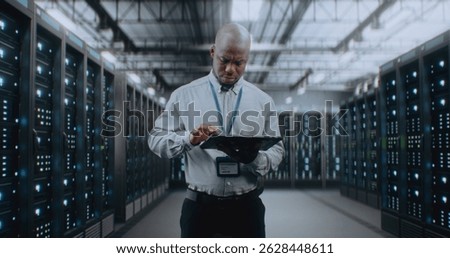 Big Data Center with Server Racks: Professional African American Specialist Using Tablet Computer, Activating Servers, Standing In Warehouse. Information Technology and Cyber Security. Medium Shot.