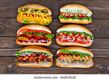 A Lot Of Big Delicious Hot Dogs With Sauce And Vegetables On Wooden Background. Their Assorted Hot Dogs To Gourmet. View From Above.