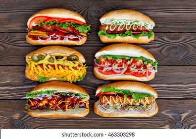 A Lot Of Big Delicious Hot Dogs With Sauce And Vegetables On Wooden Background. Their Assorted Hot Dogs To Gourmet. View From Above.