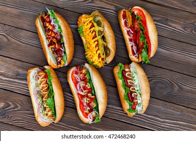 A Lot Of Big Delicious Hot Dogs With Sauce And Vegetables On Wooden Background. Their Assorted Hot Dogs To Gourmet. View From Above.