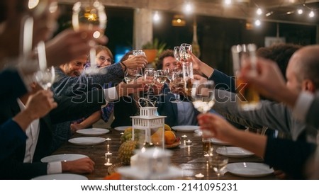 Big Dinner Party with a Small Crowd of Multiethnic Diverse Friends Celebrating at a Restaurant. Beautiful Happy Hosts Propose a Toast and Raise Wine Glasses while Sitting at a Table in the Evening.