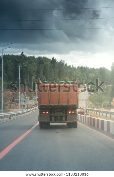 big dump truck goes in the evening on highway.\
concrete blocks on the constructed road. Metal safety barrier or\
rail on the left roadside