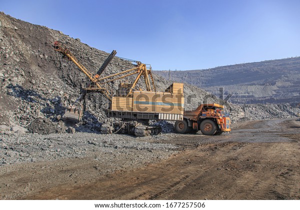 A big\
excavator in a quarry loads a big mining\
truck
