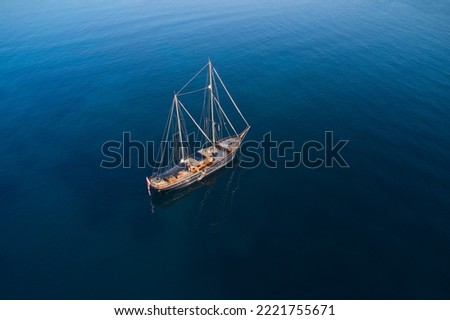 A big expensive classic yacht is anchored on blue transparent water in the rays of the sun top view. Sailing wooden yacht on the water aerial view.