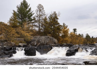 Big Falls in Wisconsin with green and yellow fall colors. Three waterfalls rush water between large boulders. - Powered by Shutterstock