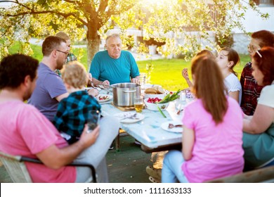 Big Familly Having A Meal Outside At The Table Under The Tree On A Beautiful Sunny Day.