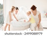 Big family with four kids in white bedroom. Parents and kids standing at crib of newborn baby boy. Mother and playing with new born child in moses basket. Kids meeting new sibling. Nursery for infant.