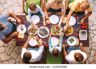 Big family have a dinner with fresh cooked meal on open garden terrace