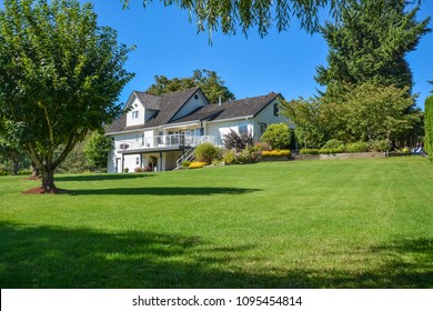 Big Family House Built  On Farm Land. Image Of Residential House On Sunny Day Framed By Green Lawn And Tree Leaves