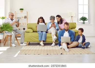 Big family sitting in living room with gadgets, parents, grandparents and two children. Grandpa, mom and grandma looking at smartphones screens, daughter and father working on laptops with son. - Powered by Shutterstock