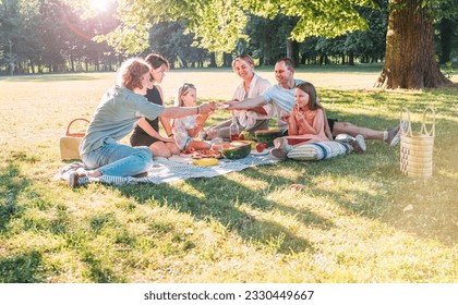 Big family sitting on the picnic blanket in city park during weekend sunny day. They smiling, laughing and eating watermelon, boiled corn,pie with cold tea. Family values, outdoors activities concept. - Powered by Shutterstock