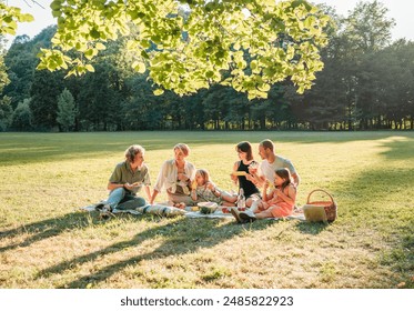 Big family sitting on the picnic blanket in city park during weekend Sunday sunny day. They are smiling, laughing and eating boiled corn and watermelon. Family values and outdoors activities concept - Powered by Shutterstock