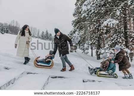 Big family spending fun time outdoors. Father pulling children on a sledge, on a cold snowy winter day.