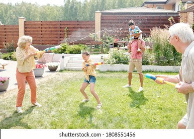 Big Family Spending Time In Backyard Shooting Water Gun On Hot Sunny Weather, Copy Space