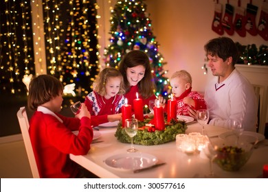 Big Family With Three Children Celebrating Christmas At Home. Festive Dinner At Fireplace And Xmas Tree. Parent And Kids Eating At Fire Place In Decorated Room. Child Lighting Advent Wreath Candle.