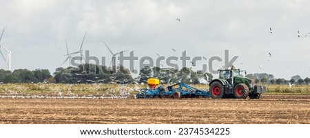 Big flock of hungry seagulls birds following modern tractor agricultural machine at farm field sowing earth or prepare soil planting seeds. North european farmland rural landscape banner