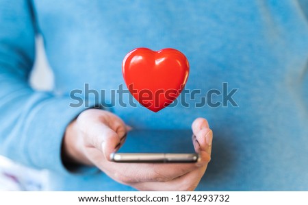 Big flying red heart. Mobile phone, smartphone in hand of man. Valentine's day holiday concept.Online love,remote communication on internet,social networks.Virtual dating,calls,technology.Coronavirus.