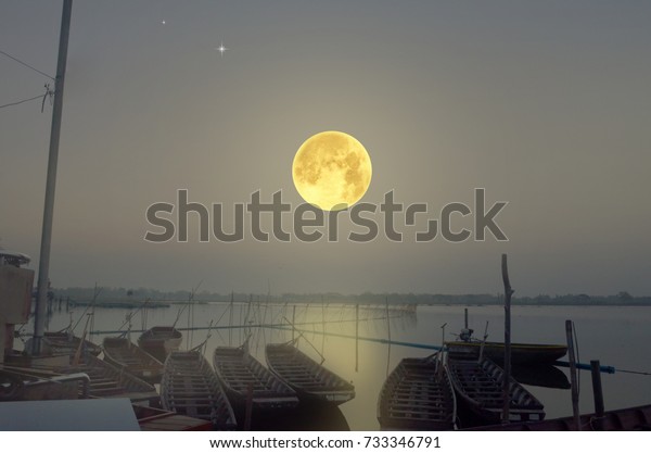 Big full moon over the\
lake and boats