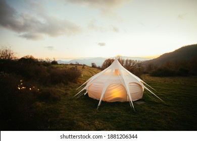 Big Glamping Camping Tent In Natural Setting At Sunset. Warm Cosy Light Inside Campground Setup Tent. Millennial Trend Vacation Destination. Staycation In Backyard In Mountains