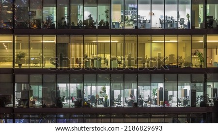 Big glowing windows in modern office buildings timelapse at night, in rows of windows light shines. People working at tables inside
