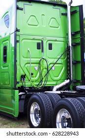 A Big Green Modern Rig Semi Truck With A High Cabin With Flat Rear Wall, A Fifth Wheel And Two Axle With New Tires On Lightweight Aluminum Rims.