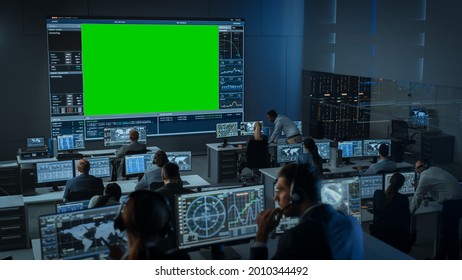 Big Green Screen Horizontal Mock Up in a Mission Control Center Room with Flight Director and Other Controllers Working on Computers. Team of Engineers Work in Monitoring Room Full of Displays. - Powered by Shutterstock