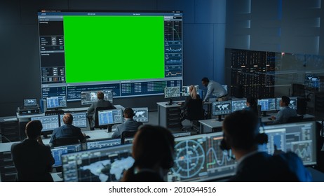 Big Green Screen Horizontal Mock Up in a Mission Control Center Room with Flight Director and Other Controllers Working on Computers. Team of Engineers Work in Monitoring Room Full of Displays. - Powered by Shutterstock