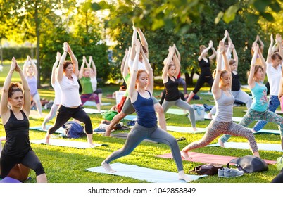 big group of adults attending a yoga class outside in park - Shutterstock ID 1042858849