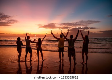 Big group of friends having fun and celebrating event with bengal fires on beach - Powered by Shutterstock