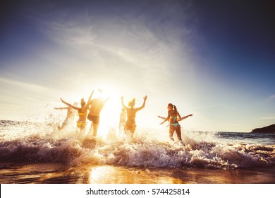 Big group of friends runs in sun light at the beach into the sea. Travel concept. Space for text - Shutterstock ID 574425814