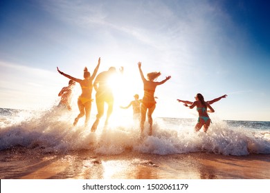 Große Gruppe von sieben glücklichen Freunden hat Spaß und läuft bei SonnenunterSonnenuntergang Strand zu Sonne und Wellen