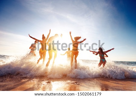 Big group of seven happy friends is having fun and runs at sunset beach to sun light and waves