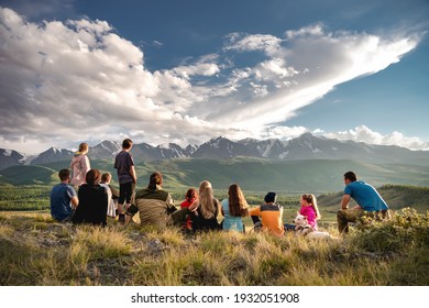 Big group of tourists are sitting and relaxing at hilltop and looking at sunset mountains