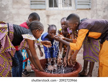 Big Group Of Young African Ethnicity Children Playing With And Pouring Water From Bucket In A Poor Village In Mali
