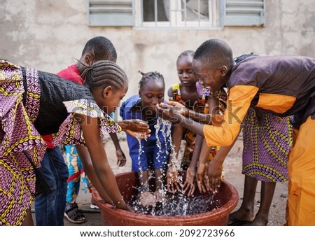 Big group of young African ethnicity children playing with and pouring water from bucket in a poor village in Mali