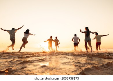 Big Group Of Young Friends Or Big Family Are Having Fun And Run At Sunset Beach. Summer Vacations Concept