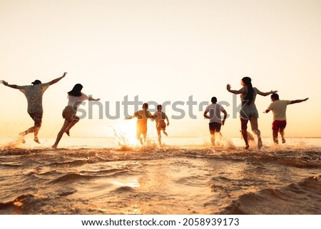 Big group of young friends or big family are having fun and run at sunset beach. Summer vacations concept