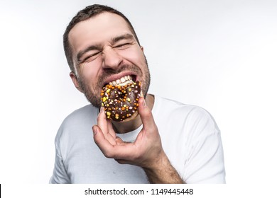 Big guy is starving. He decided to eat tasty small fat donut covered with chocolate. He is biting it with delisions feeling and pleasure. Isolated on white background.