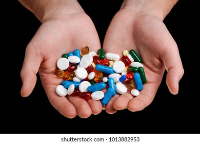 Big handful of tablets, capsules and softgels in cupped hands on black background. Wide range of medicaments.